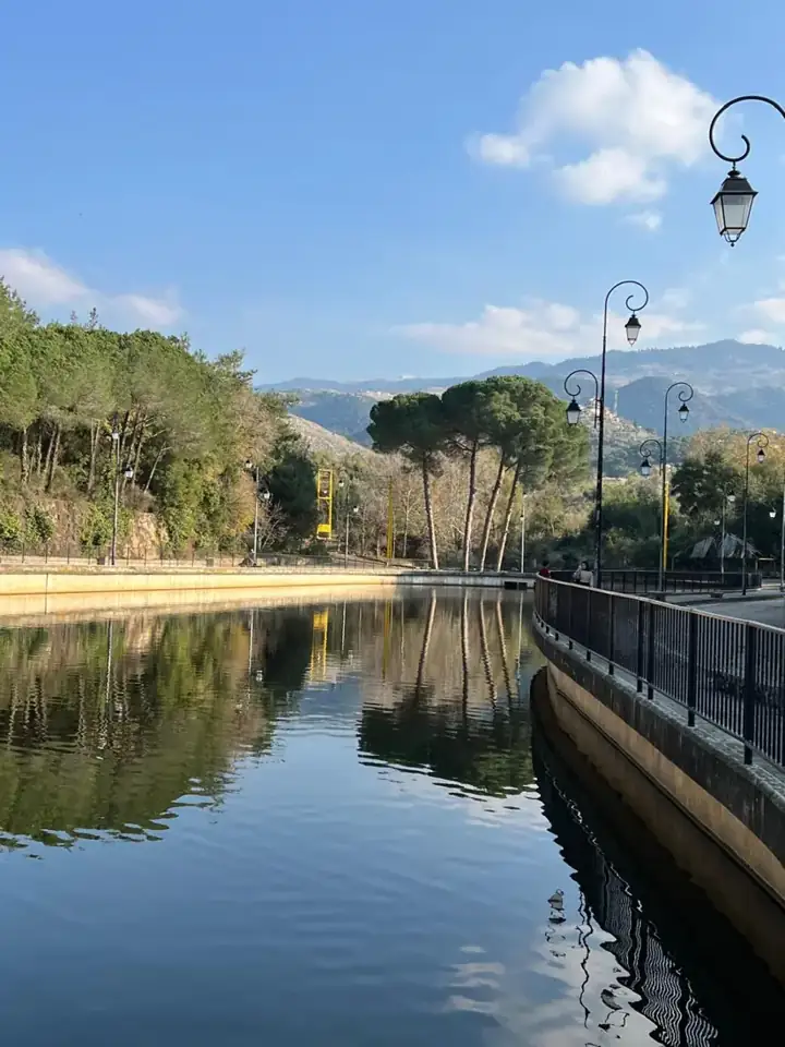 Water channel lined with trees and street lamps below the mountains